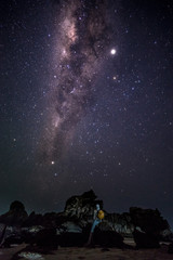 Fototapeta na wymiar Person enjoys amazing magical milky way galaxy night sky nearby rock formations at the beach