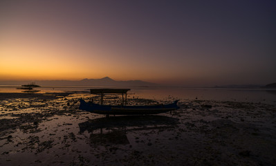 Wooden traditional fishing boat stuck on low tide at the beach on vivid colorful sunset at Jelenga beach, Sumbawa