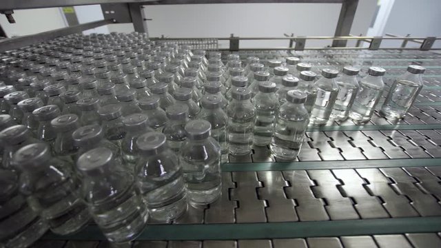 glass bottles filled and sealed with rubber and aluminum caps on medical solution conveyor line medical industry