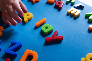 Child hand playing with colorful letters spelling Play
