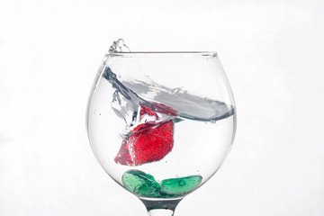 A splash in a glass of liquid on a light background with red pieces of ice. The pieces are covered with air bubbles. Backgrounds and textures.