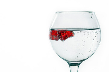 A glass of liquid on a light background with red pieces of ice. The pieces are covered with air bubbles. Backgrounds and textures.