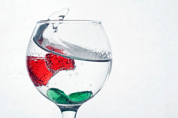 A splash in a glass of liquid on a light background with red pieces of ice. The pieces are covered...