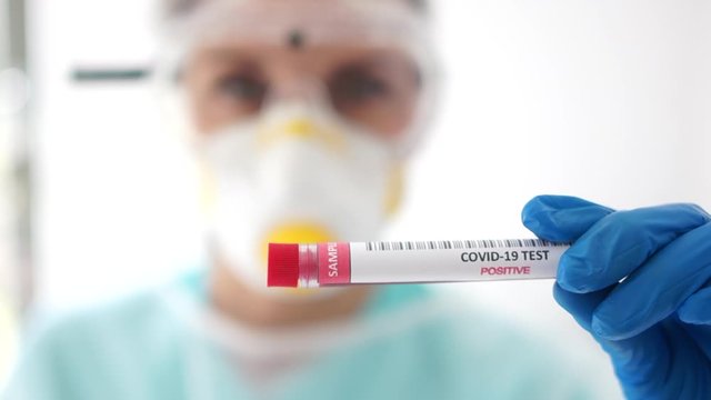Positive coronovirus test. Female doctor in goggles and a mask holds a test tube with a blood sample of infected covid-19