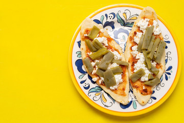 Mexican tlacoyos with nopal cactus and cheese on yellow background