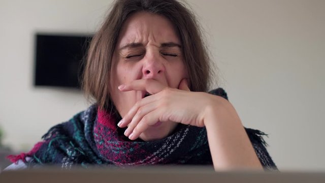 Tired woman working on laptop and yawns. Stressed girl proping head, touching and wrying face.