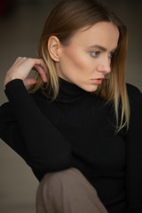 Fototapeta premium close up portrait of stylish looking girl in black turtleneck with blue eyes, model posing in interior, studio background 