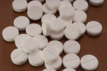 White tablets are scattered from a bottle on a brown background.