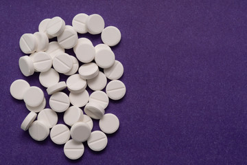 Fototapeta na wymiar White tablets are scattered from a bottle on a purple background.