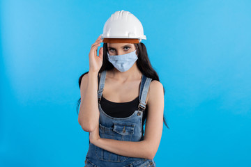 A young woman at a construction site wearing a helmet and a protective mask waits for orders from her superiors.