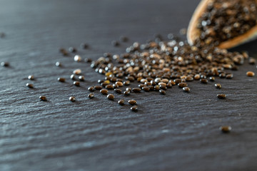 Food chia seeds in wooden spoon. Healthy pile flax superfood on black background. Salvia hispanica antioxidant grains on stone dark texture.