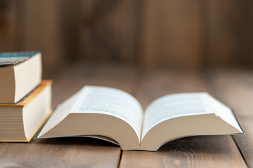 A hardback book opened for reading and two large books stacked on the right