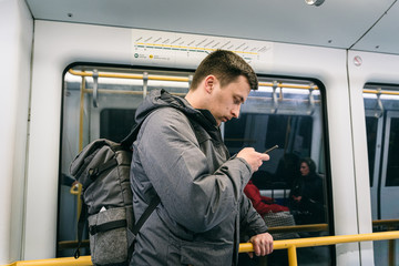 Caucasian male tourist with a backpack in the subway Copenhagen, Denmark. Side view of man with rucksack and smartphone at metro. Passenger takes underground watching his smartphone