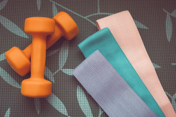 Orange dumbbell for fitness and sports elastic bands on a grey background, concept of home workouts