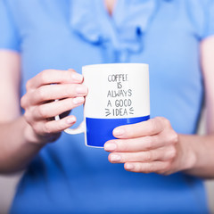 Female hands holding white blue cup with inscription. Coffee is always a good idea. Break time concept