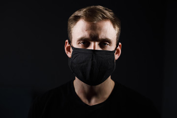 Handsome man in black t-shirt wear black medical mask, gray background. Coronavirus covid-19...