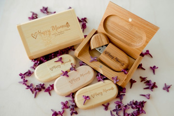Wooden brown usb flash drives with boxes with the text Happy Moments with lilac petals on a white background, data storage, beautiful feedback to client.