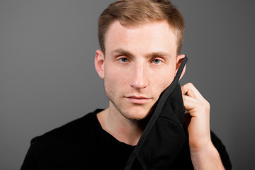 Handsome man in black t-shirt wear black medical mask, gray background. Coronavirus covid-19 quarantine period concept.