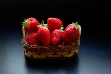 strawberries in a braided basket on the black table