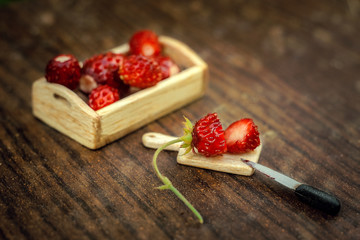 Strawberry berry on a wooden miniature Board, cut with a miniature knife.Next to it is a wooden tray with berries.Soft focus
