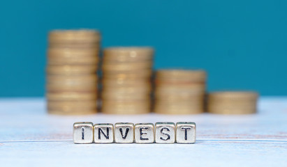 word INVEST and coins on wooden background. Funding and business concept.