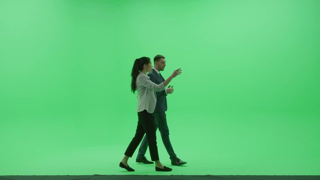 Chroma Key Studio: Beautiful Woman wearing Business Casual Talks with Handsome Businessman, They Discuss Business, Financial Consulting and Walking Across the Green Screen Room. Side View Shot