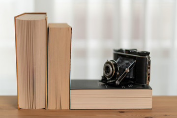 There are three books on the shelf in front of the window curtain. An old analog camera