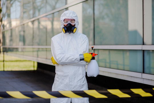 Stop coronavirus. Portrait of man in white protection suit with mask and sprayer holding arms up and celebrating successful city disinfection.