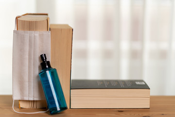 There are three books on the shelf in front of the window curtain, one spray cologne, one surgical mask on the shelf. 