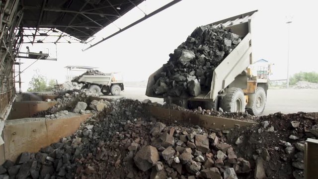 Heavy dump trucks Belaz unload granite stones on the granite crushing line slow motion.