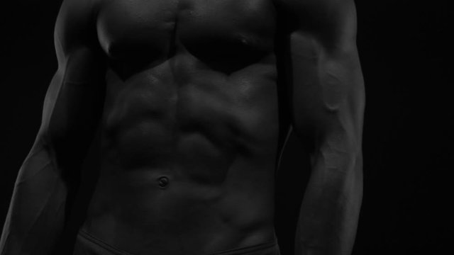 Strong bodybuilder posing and training in contrast light showing his body and every muscle on it under water drops and slow rain
