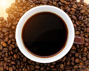 Coffee cup on wooden kitchen table with coffee beans. Top view with morning sunlight
