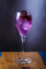 Delicious alcoholic cocktail with pieces of ice, a large mulberry in a transparent glass on a long leg. Copy space