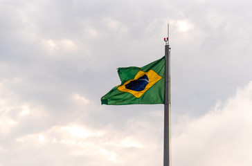 Flag of Brazil fluttering in the wind hoisted on iron mast on light and outdoors background
