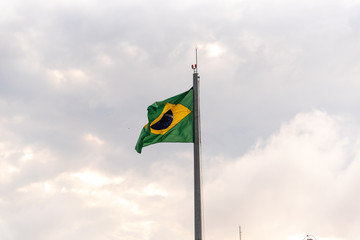 Flag of Brazil fluttering in the wind hoisted on iron mast on light and outdoors background
