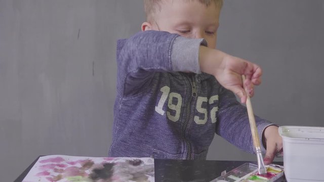 A child funny boy with cut face is drawing with colored paints