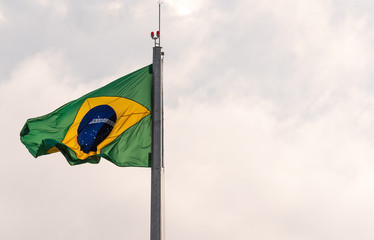 Flag of Brazil fluttering in the wind hoisted on iron mast on light and outdoors background