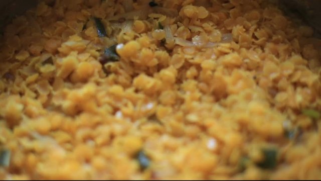 Focus changing blurry rotating close up of cooked hot smoking yellow dhal curry in pot with curry leaves in sri lanka.