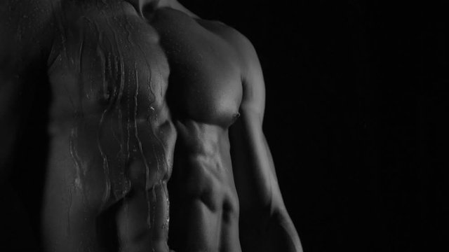 Strong bodybuilder posing and training in contrast light showing his body and every muscle on it under water drops and slow rain