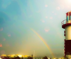 rainbow fantasy with blue sky, black white and red lighthouse and beautiful colors over harbor...
