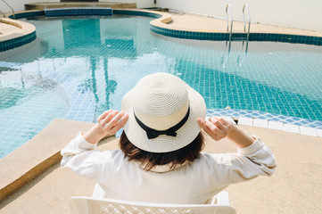 Obraz premium Back view of woman relaxing and sitting nearly swimming pool in hotel. This pool designed to hold water for leisure activities. Conceptual of tourist woman lifestyle.