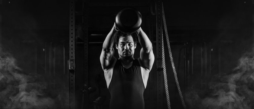 asian athletic strong man having workout and bodybuilding with kettlebell weightlifting backsquat style in gym and fitness center in dark tone black and white