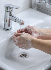 Hand washing with soap. Preventive measures against infection. A young guy washes his hands with soap in the bathroom. Body hygiene. The fight against COVID-19.