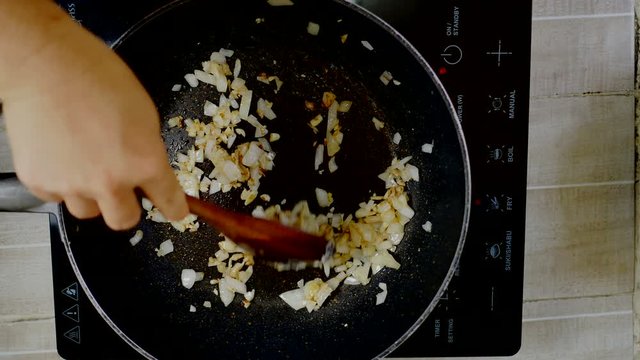fried garlic and onion with wooden turner in induction pan on electric stove, red light indicator power on and fry menu button, high temperature