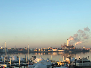 Sunrise over waterfront industrial center with smoke  blowing from factory smoke stacks in Baltimore Maryland on Potomac harbor waterfront with yachts in foreground - obrazy, fototapety, plakaty