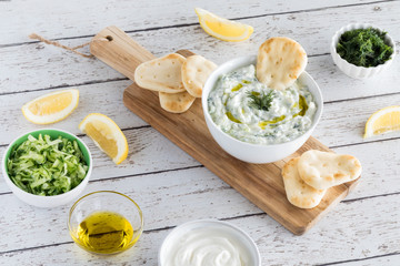 Top down view of tzatziki dip surrounded by ingredients used to make the dip and pita bites for dipping.