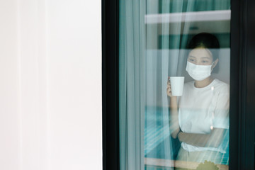 Sick asian female of corona virus looking through the window and wearing mask protection and recovery from the illness in home. Quarantine. Patient isolated to prevent infection.