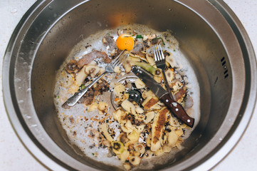 A metal sink in which there are two forks, a knife with a wooden handle and potato peel. The concept of vegetable waste in the cooking process.