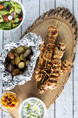 Flat lay view of grilled chicken skewers with baby potatoes, tzatziki dip and Greek salad.