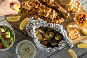 Top down arrangement of barbecue Greek cuisine dishes with a hand squirting lemon juice. 